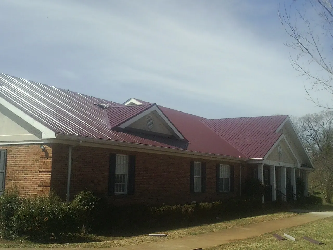 Red metal roof with gabled entries on a long brick building, from a Hail Damage Roof Repair job in Defiance