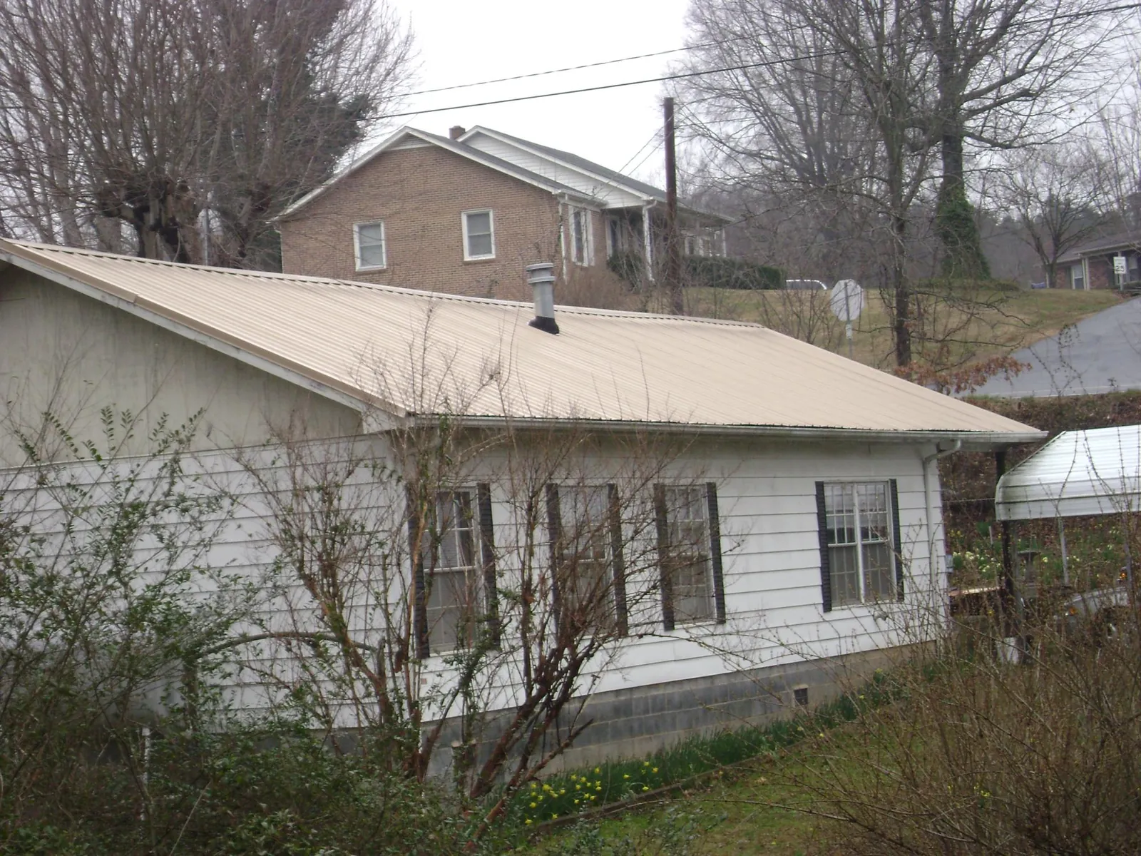Tan metal roof on a white sided house set into a hillside — Commercial Roofing by Roofing Brothers in Defiance